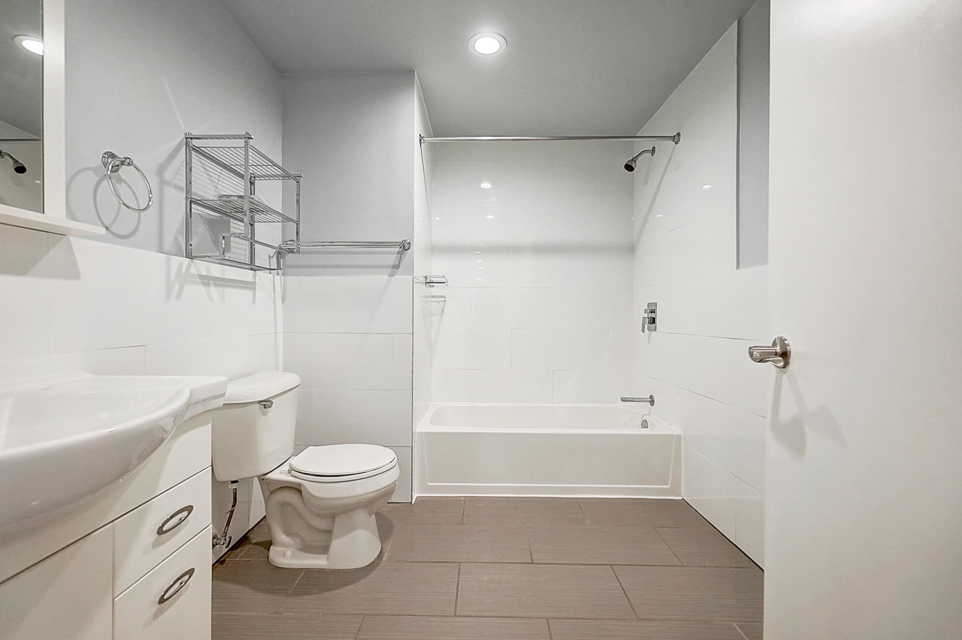 Bathroom with a white vanity on the left, a toilet, a bathtub across the back wall, white tiled walls and gray floor tiles.