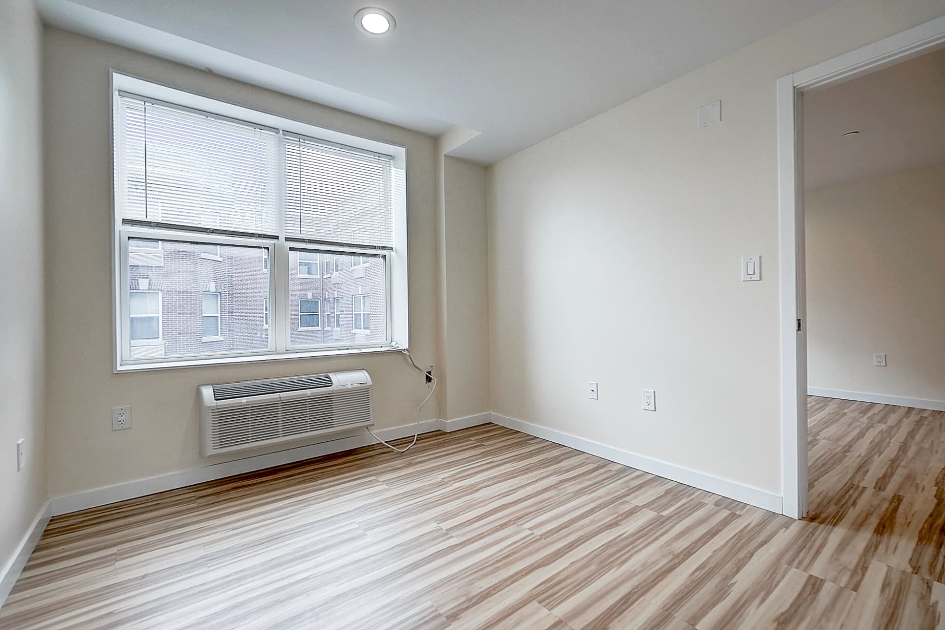 Unfurnished room with a large window and blinds, an air conditioner below, wood-pattern flooring and an open doorway on the right.